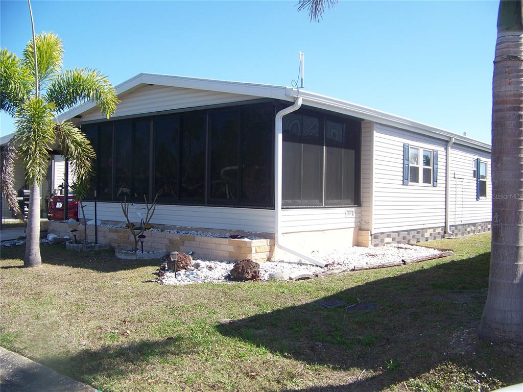 A single-story manufactured home features a screened-in porch, light siding, and a landscaped yard — 15550 BURNT STORE ROAD UNIT 72, PUNTA GORDA, FL