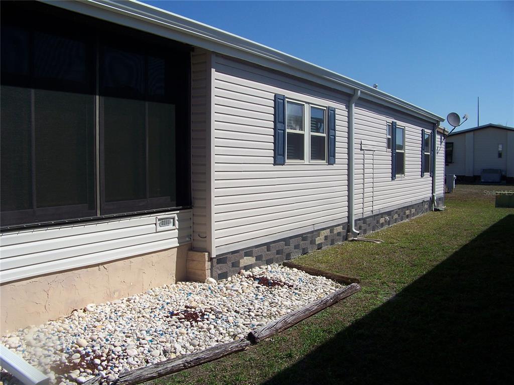 The exterior side of a manufactured home features light siding, blue shutters, and stone skirting — 15550 BURNT STORE ROAD UNIT 72, PUNTA GORDA, FL