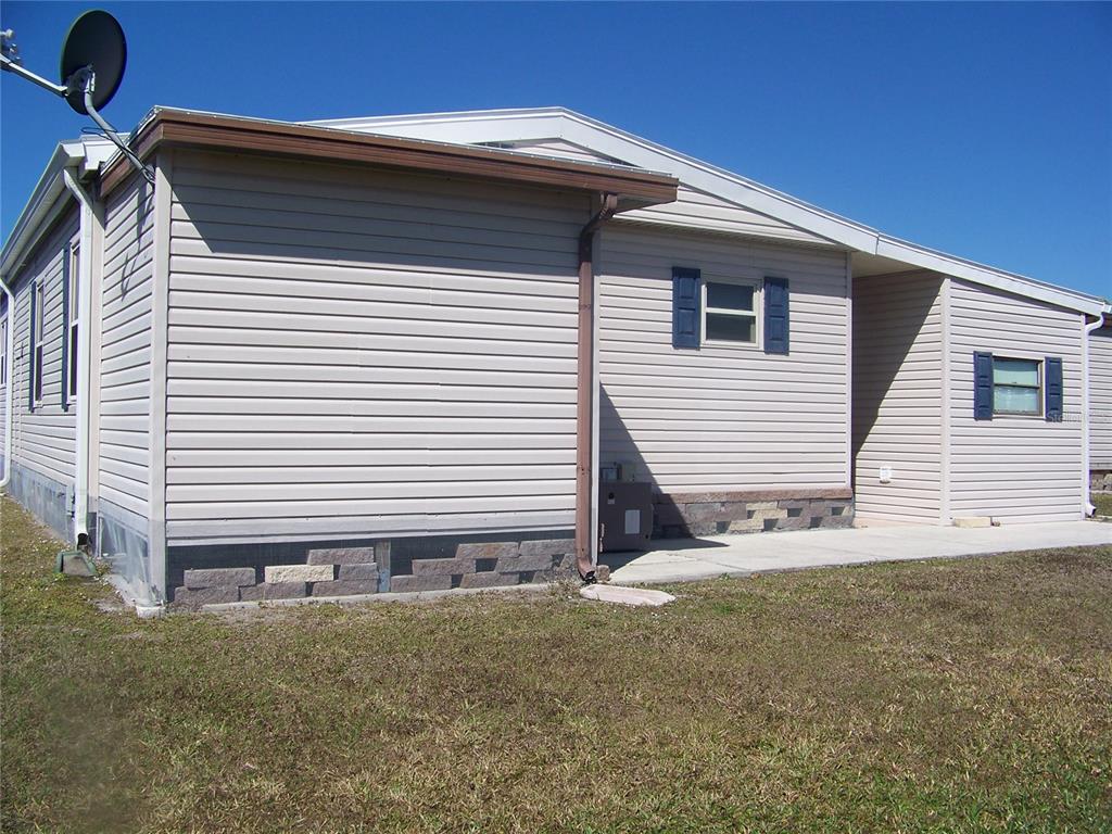 The exterior of a beige, single-story manufactured home with a stone-veneer skirting and concrete patio — 15550 BURNT STORE ROAD UNIT 72, PUNTA GORDA, FL