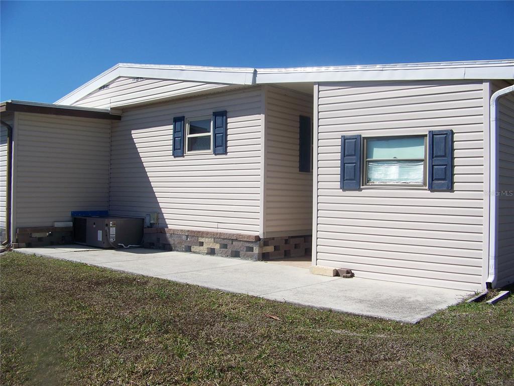 The exterior of a beige mobile home features blue shutters and a concrete patio area — 15550 BURNT STORE ROAD UNIT 72, PUNTA GORDA, FL