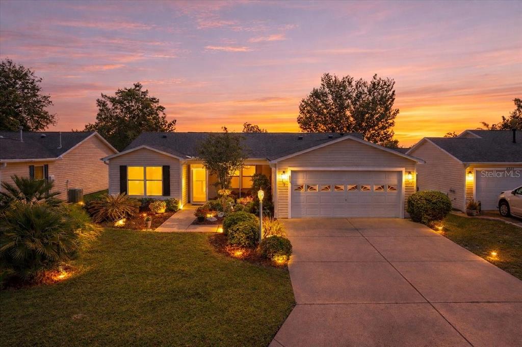 A single-story house with a two-car garage and a landscaped front yard at sunset — 8354 SE 177TH BARTRAM LOOP, THE VILLAGES, FL