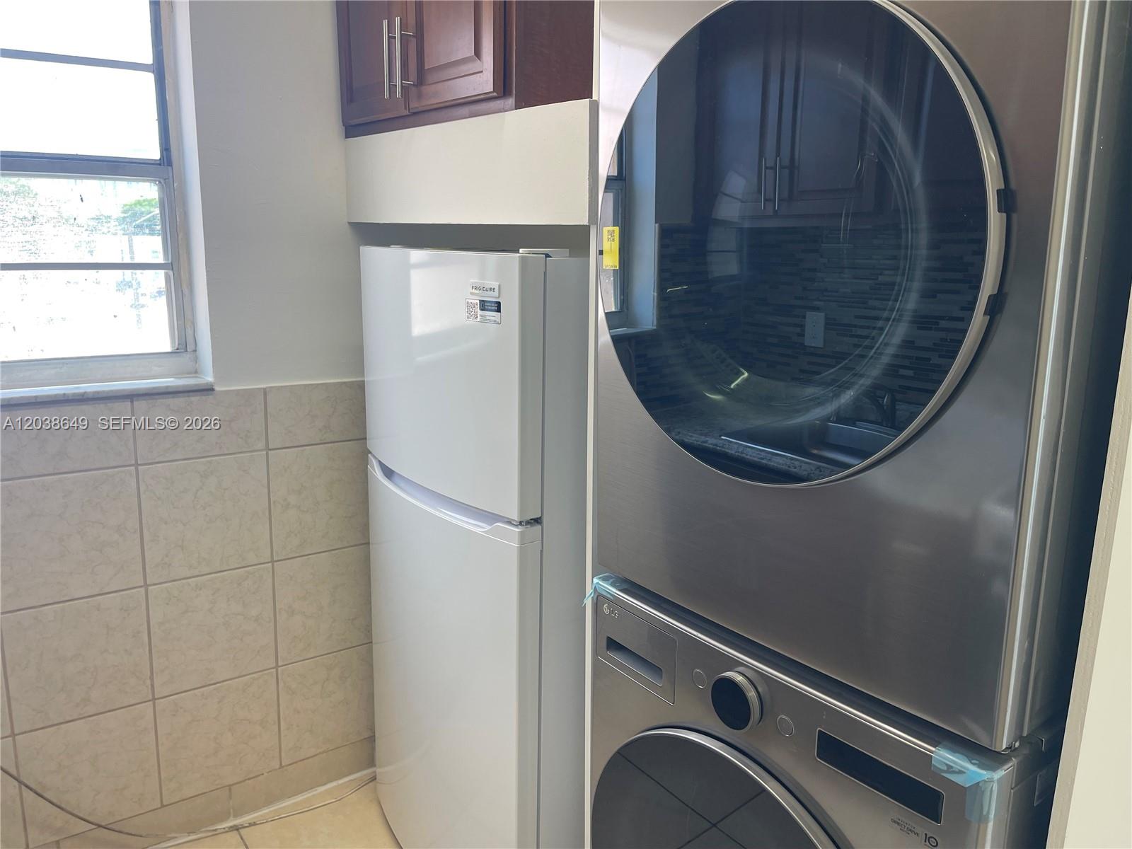 A white refrigerator stands next to a stacked stainless steel washer and dryer unit — 1043 NW 2nd St # 14, Miami FL 33128, MIAMI, FL