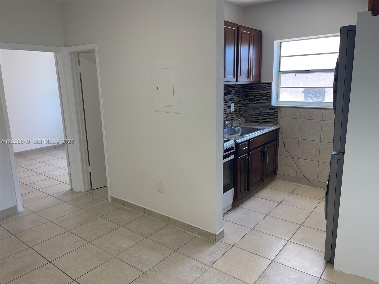 A small kitchen features dark wood cabinets, a tiled backsplash, and light-colored floor tiles — 1043 NW 2nd St # 14, Miami FL 33128, MIAMI, FL