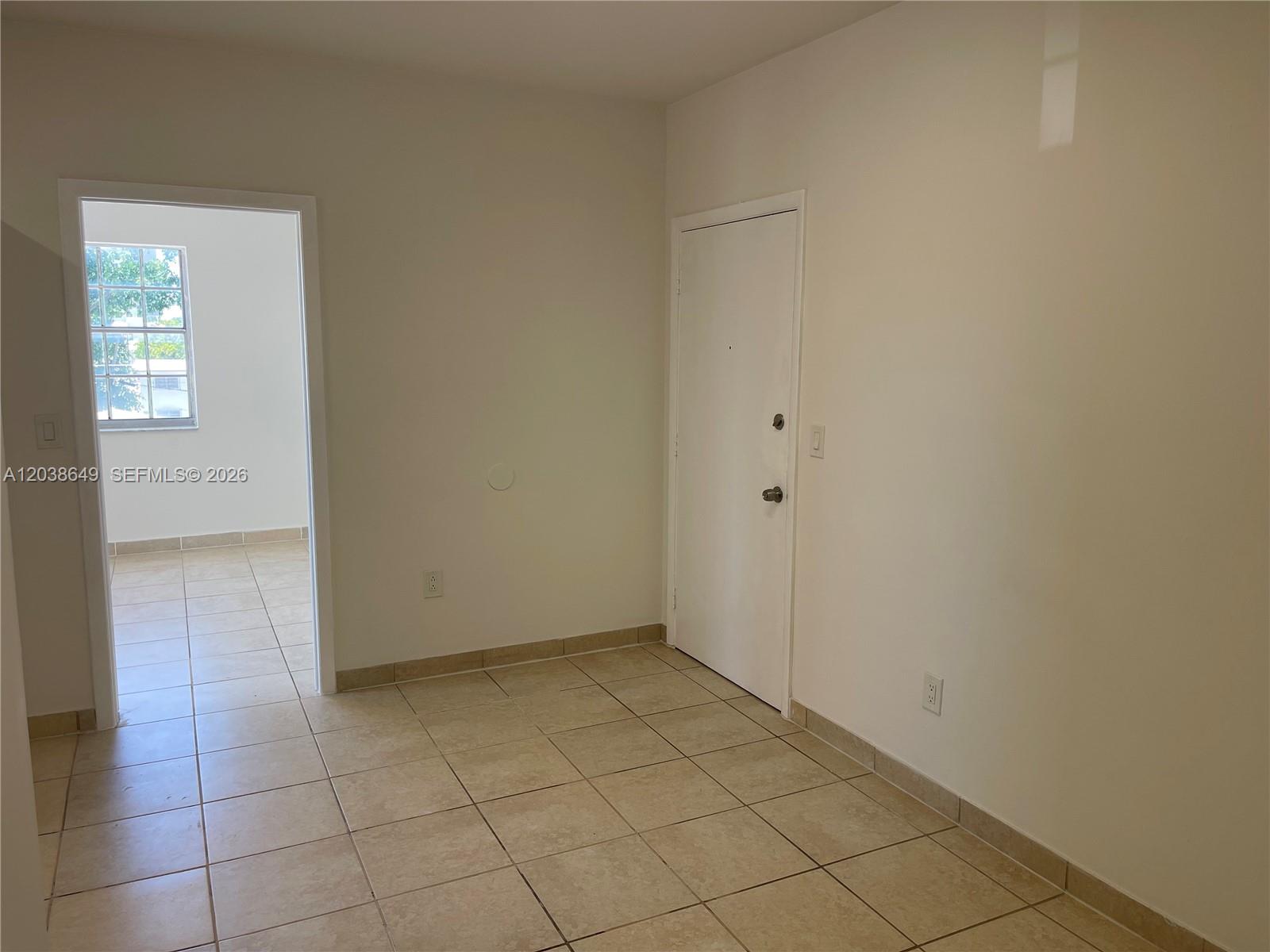 An empty room with beige tile flooring, white walls, and a closed white door — 1043 NW 2nd St # 14, Miami FL 33128, MIAMI, FL