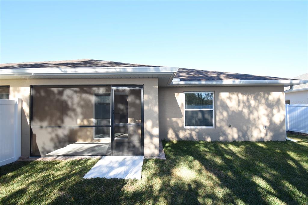 The exterior rear view of a house features a screened-in patio and a grassy yard — 11 BUTTONWOOD LANE UNIT A, PALM COAST, FL