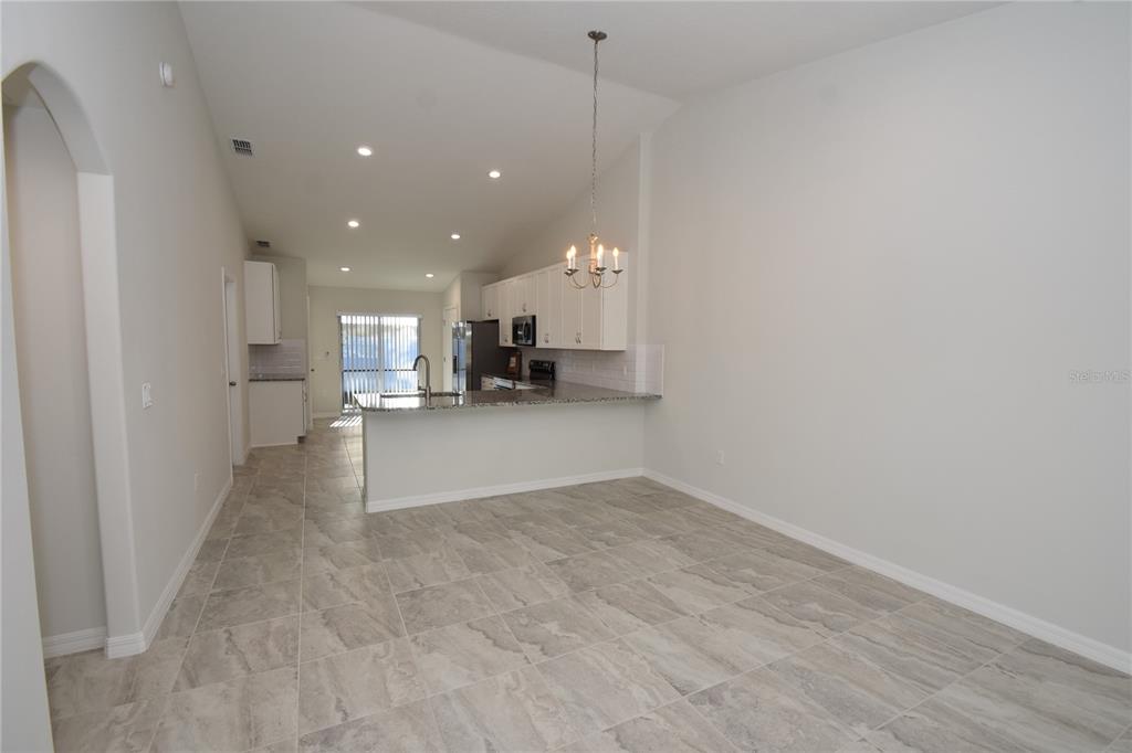 An open-concept kitchen features white cabinets, granite countertops, and light-colored tile flooring — 11 BUTTONWOOD LANE UNIT A, PALM COAST, FL