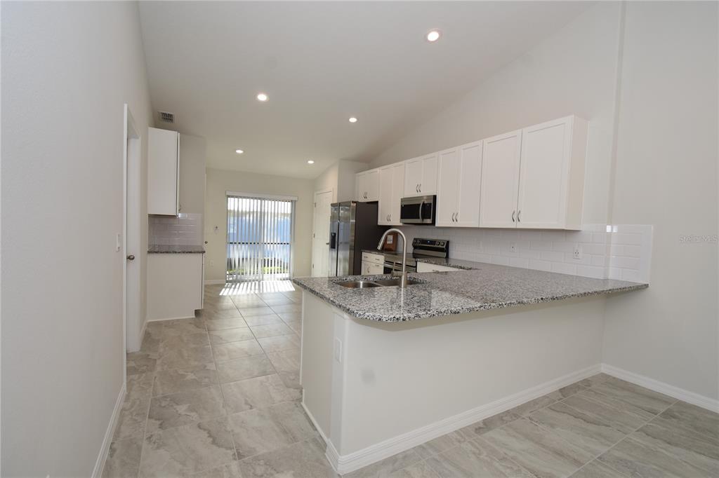 A kitchen features white cabinets, granite countertops, a stainless steel microwave, and light tile flooring — 11 BUTTONWOOD LANE UNIT A, PALM COAST, FL