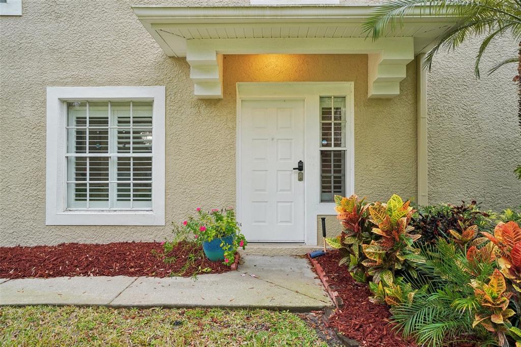A white front door with a smart lock sits under a small porch overhang — 2243 ANDOVER CIRCLE, PALM HARBOR, FL