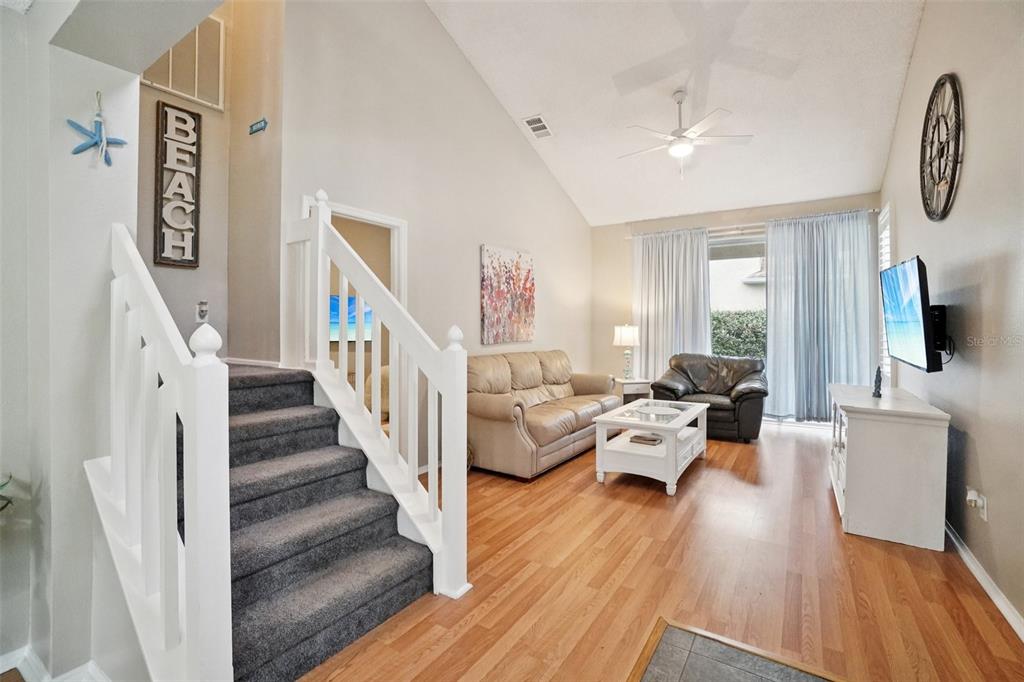 A living room features a vaulted ceiling, wood flooring, a staircase, and a beige sofa — 2243 ANDOVER CIRCLE, PALM HARBOR, FL