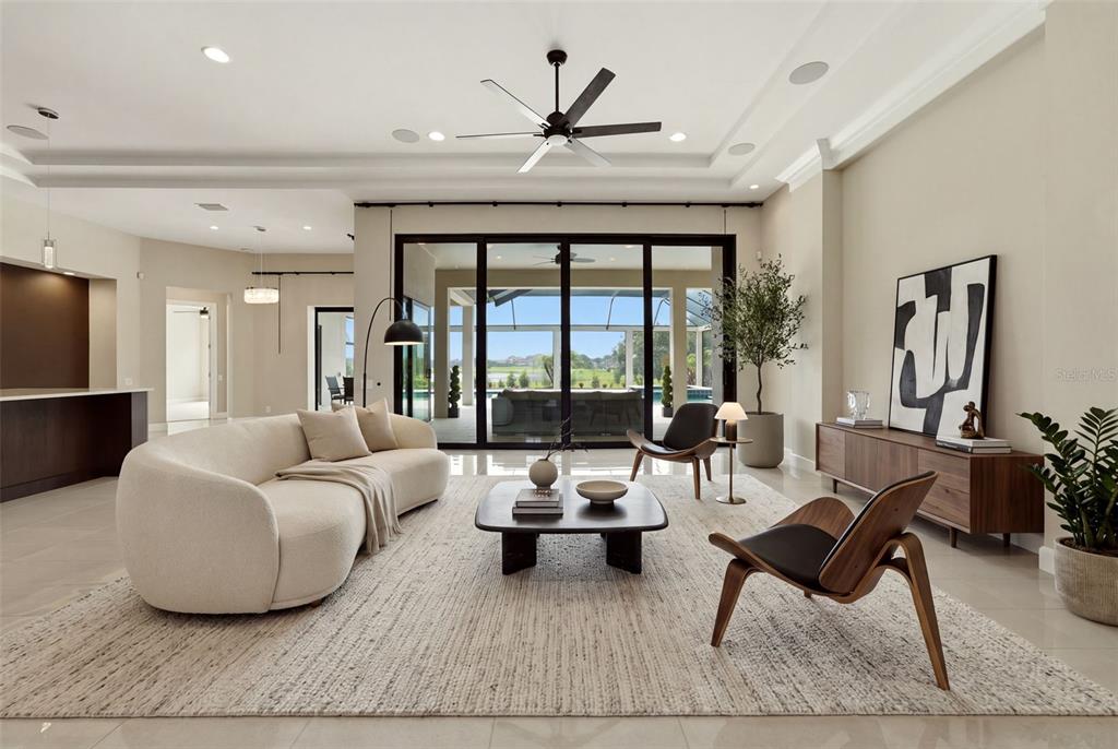 A modern living room features a curved sofa, wooden chairs, and large sliding glass doors — 10741 OSPREY LANDING WAY, THONOTOSASSA, FL
