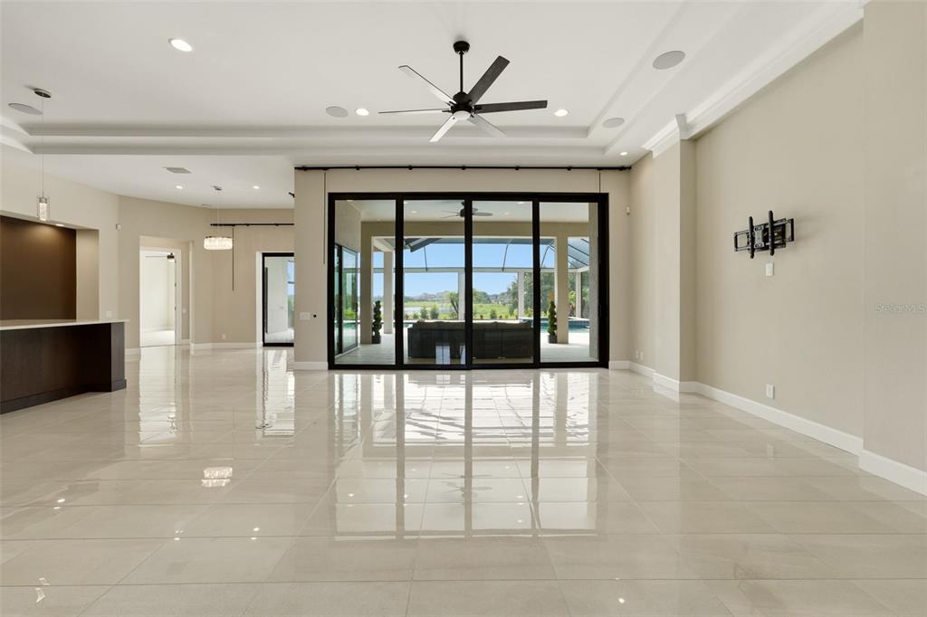 A spacious living room features large sliding glass doors, a ceiling fan, and tile flooring — 10741 OSPREY LANDING WAY, THONOTOSASSA, FL