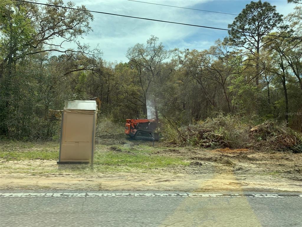 A construction vehicle clears brush on a wooded lot next to a portable toilet — 2564 W MUSTANG BOULEVARD, BEVERLY HILLS, FL