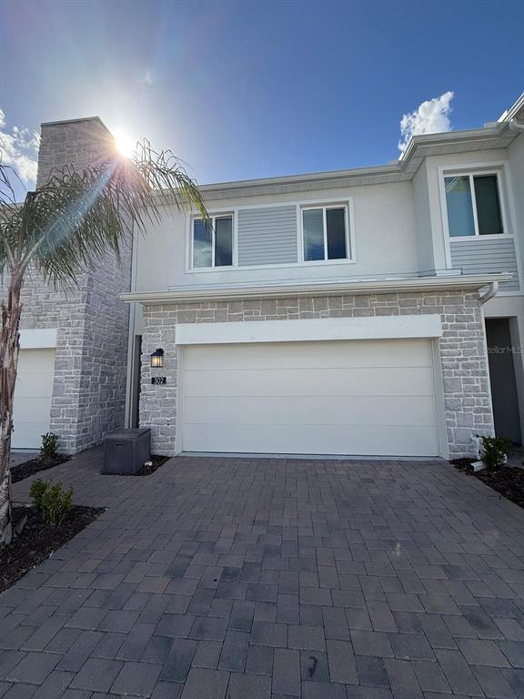 A two-story townhouse exterior features a stone facade, a two-car garage, and a paver driveway — 502 BOGEY DRIVE, DAVENPORT, FL