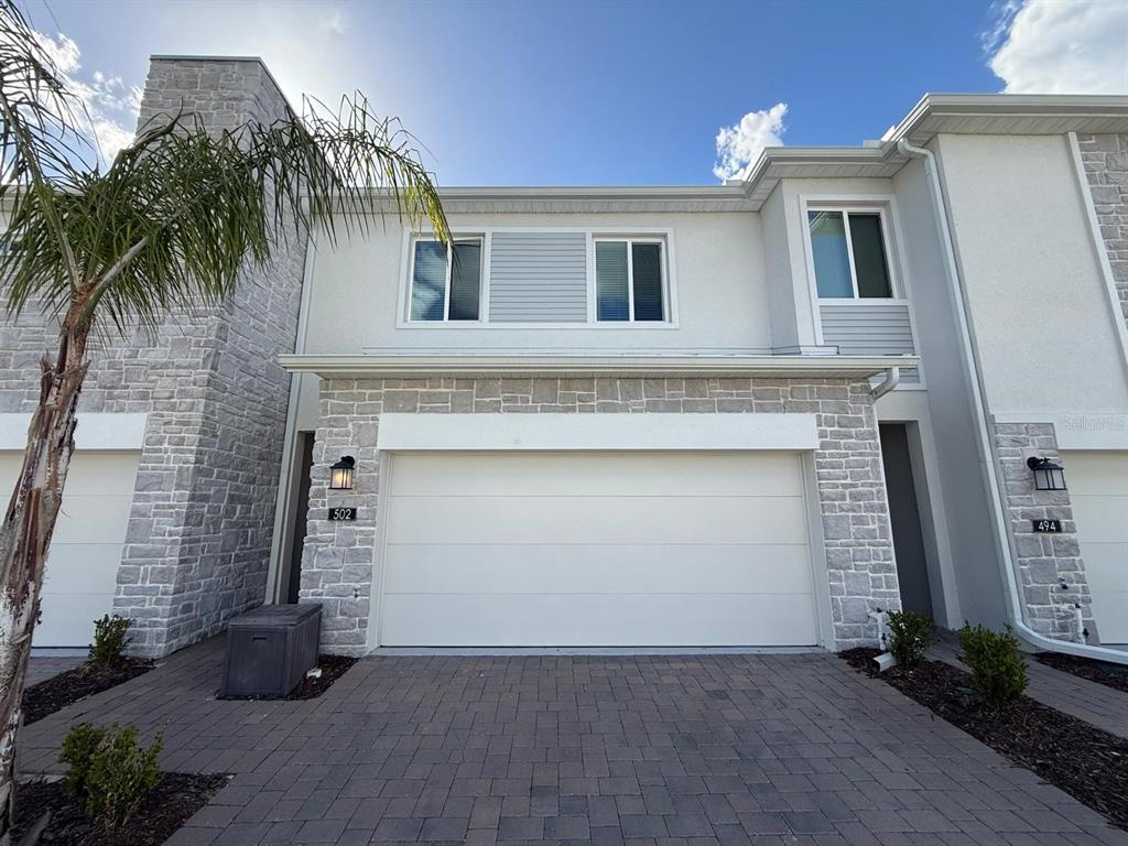 A two-story townhouse exterior features a stone facade, a two-car garage, and a paved driveway — 502 BOGEY DRIVE, DAVENPORT, FL
