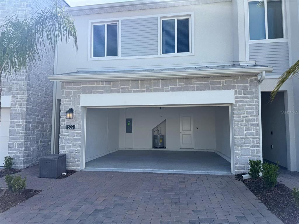 A two-story townhouse exterior features a stone-faced facade, a single-car garage, and a paved driveway — 502 BOGEY DRIVE, DAVENPORT, FL