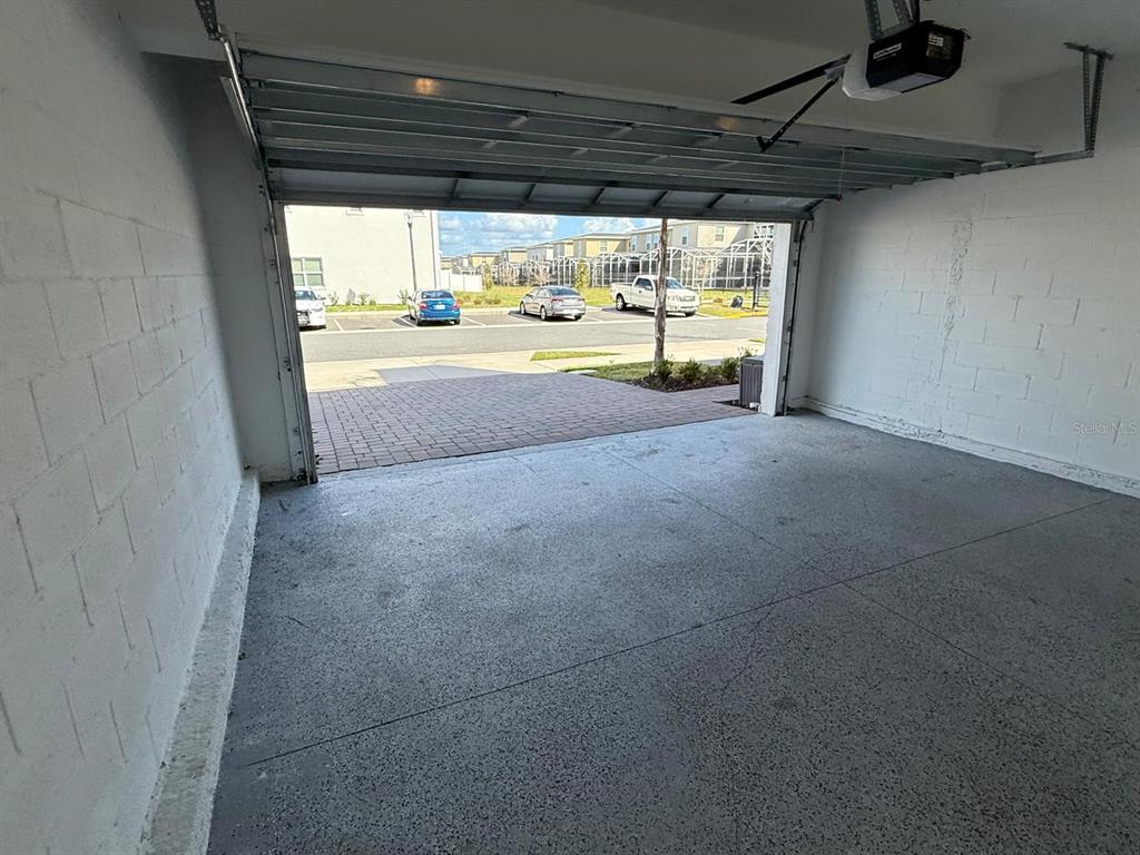 An open garage with a concrete floor, white block walls, and a view of parked cars — 502 BOGEY DRIVE, DAVENPORT, FL