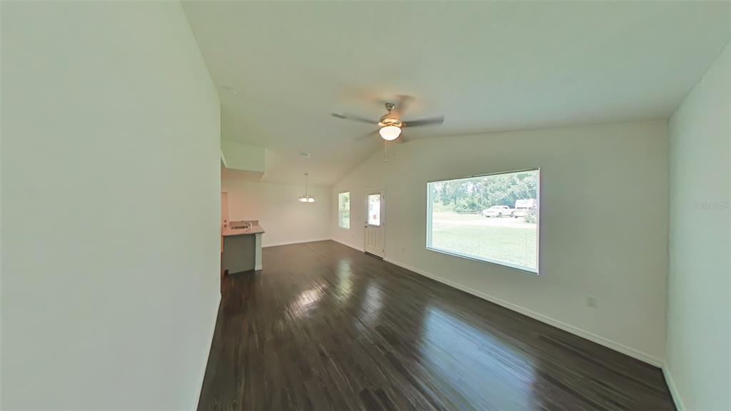 An open-concept living area features dark wood-look flooring, a vaulted ceiling, and a large window — 3780 SE 141ST LANE, SUMMERFIELD, FL