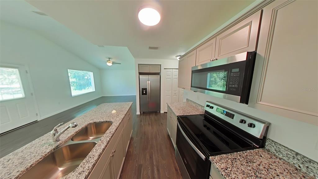 A kitchen features granite countertops, stainless steel appliances, and light-colored cabinetry with dark wood flooring — 3780 SE 141ST LANE, SUMMERFIELD, FL