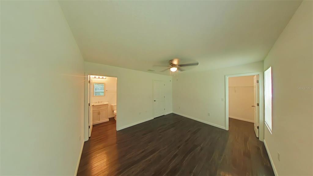 A bedroom with dark wood flooring, a ceiling fan, an attached bathroom, and a walk-in closet — 3780 SE 141ST LANE, SUMMERFIELD, FL