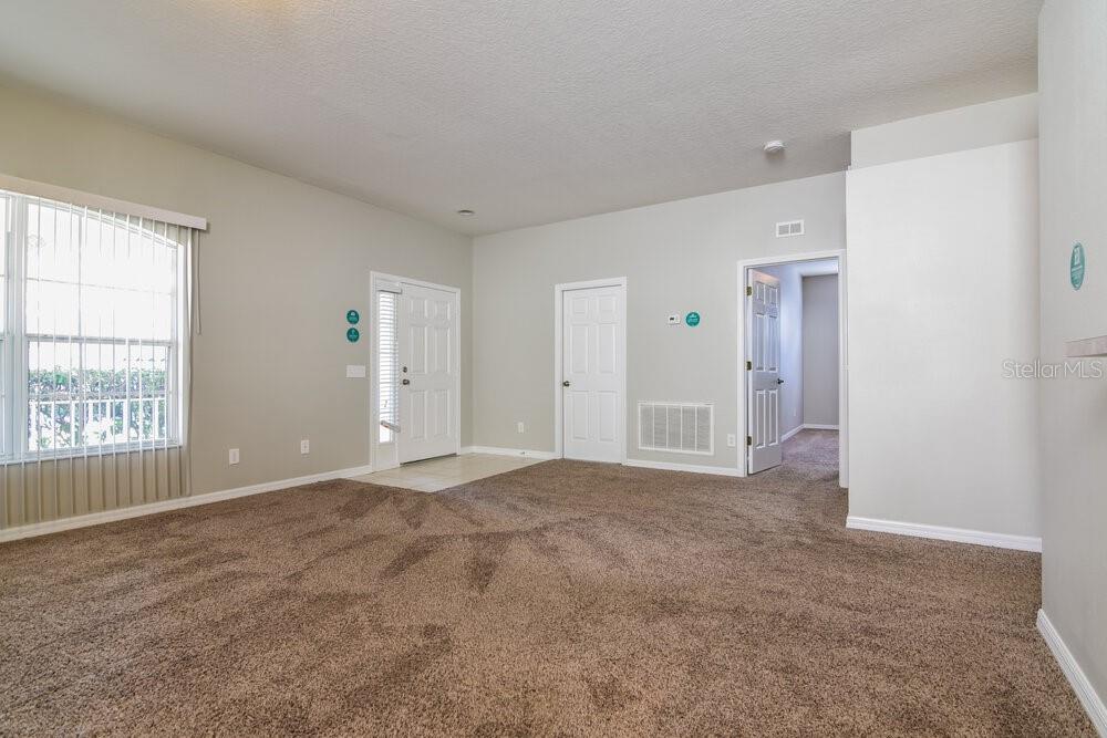 An empty living room with beige carpet, light-colored walls, a front door, and interior doors — 15819 STAGS LEAP DRIVE, LUTZ, FL