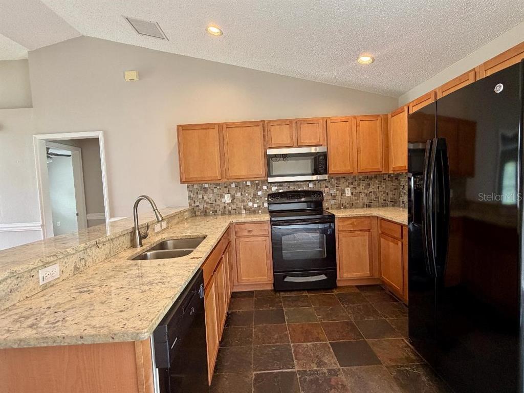 A kitchen features oak cabinets, granite countertops, a tile backsplash, and black appliances — 881 HANFORD DRIVE, DELTONA, FL