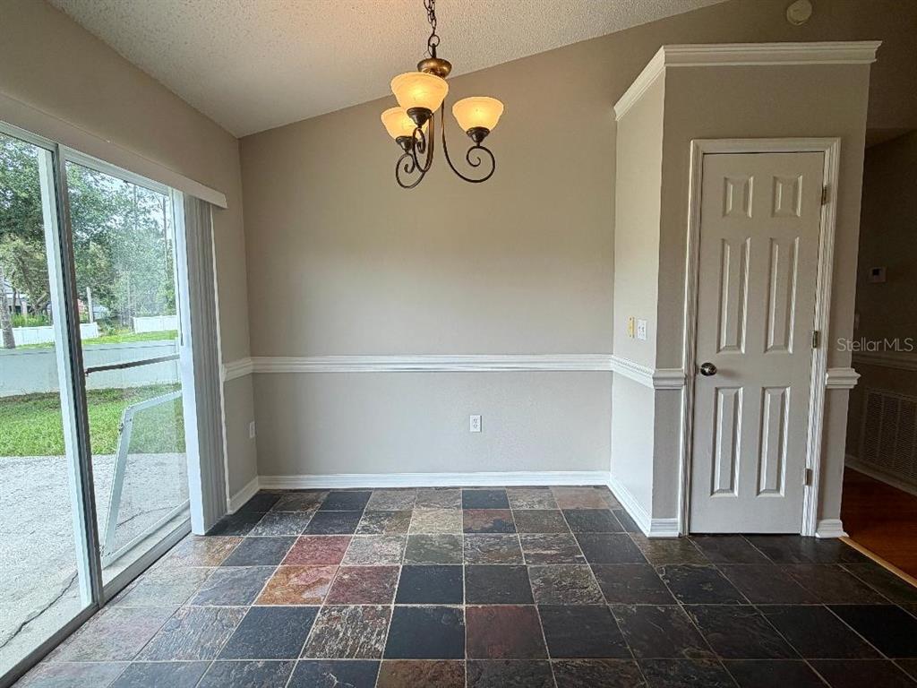 A dining area features a slate tile floor, a chandelier, and a sliding glass door — 881 HANFORD DRIVE, DELTONA, FL
