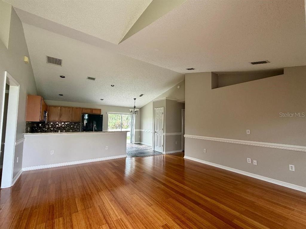 A living room with hardwood floors opens to a kitchen with wood cabinets — 881 HANFORD DRIVE, DELTONA, FL