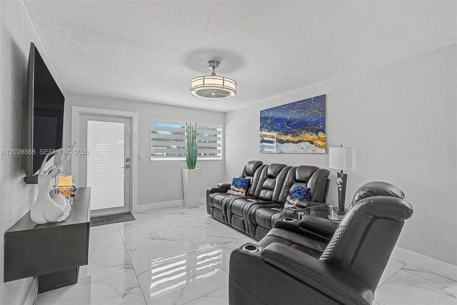 A living room features white marble-look tile floors, black leather reclining furniture, and a ceiling fan — 10345 NW 35th Ct, Miami FL 33147, MIAMI, FL