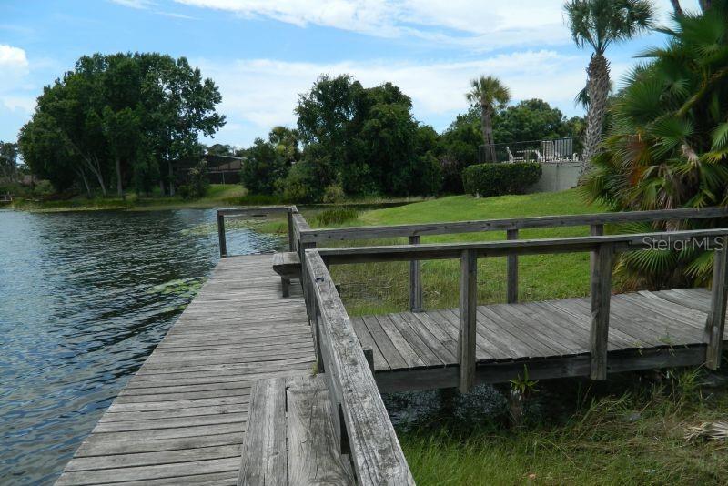 A wooden dock with a built-in bench extends over a lake near a grassy yard — 922 LAKE DESTINY ROAD UNIT E, ALTAMONTE SPRINGS, FL