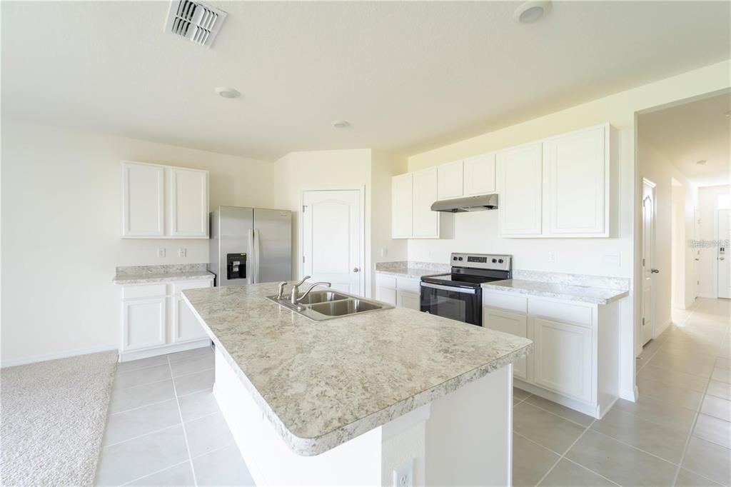 A kitchen features white cabinets, granite countertops, a central island with a sink, and appliances — 1811 SILVERBELL LOOP, HAINES CITY, FL