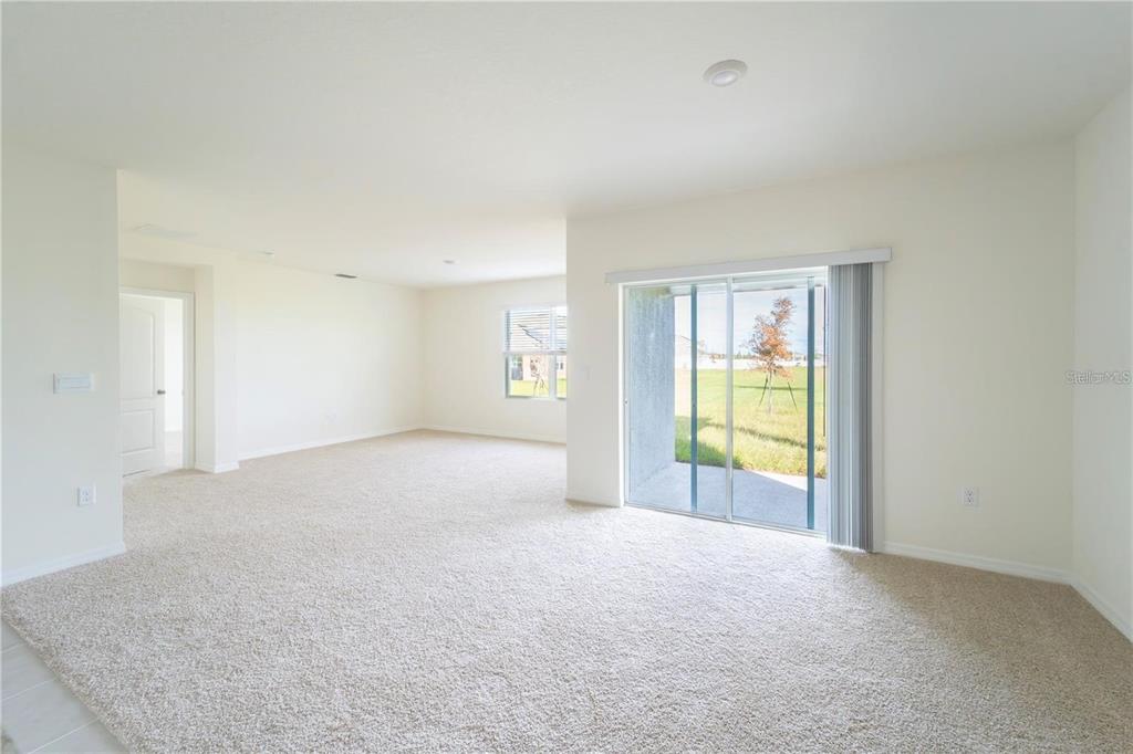An empty living room with beige carpet, white walls, and a sliding glass door — 1811 SILVERBELL LOOP, HAINES CITY, FL