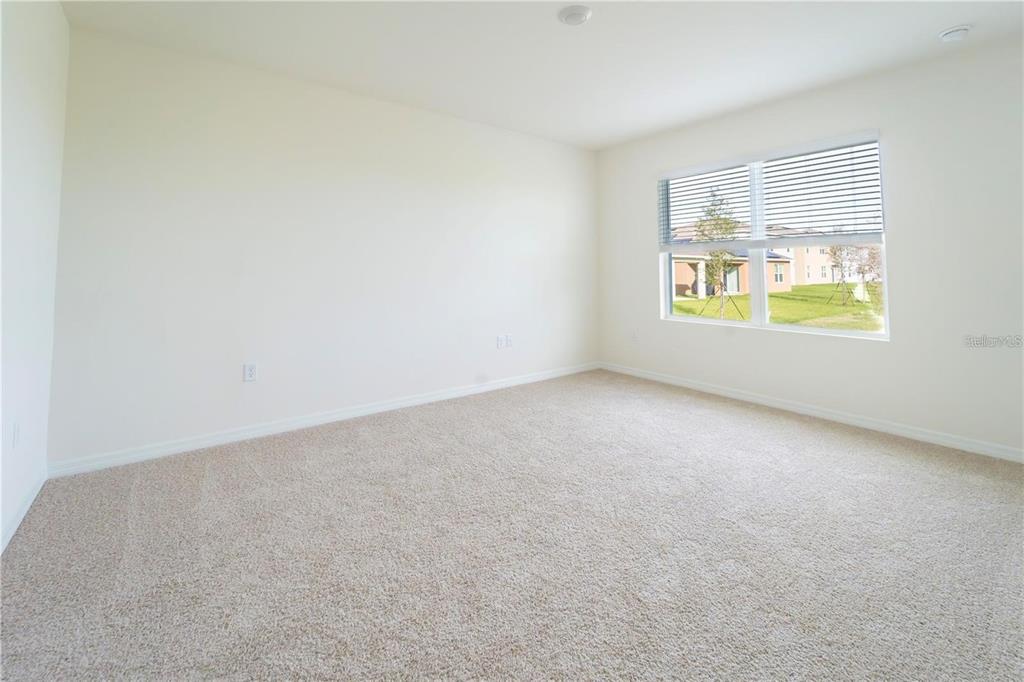 An empty bedroom features beige carpet, off-white walls, and a window overlooking a grassy area — 1811 SILVERBELL LOOP, HAINES CITY, FL