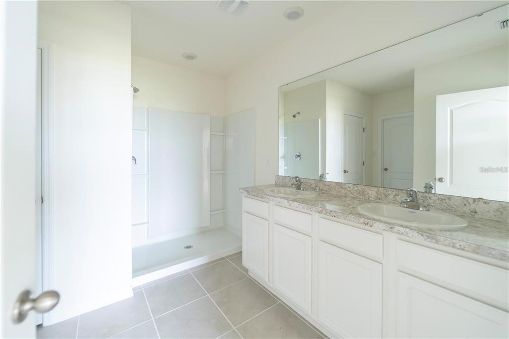 A bathroom features a double vanity with a stone countertop and a walk-in shower — 1811 SILVERBELL LOOP, HAINES CITY, FL