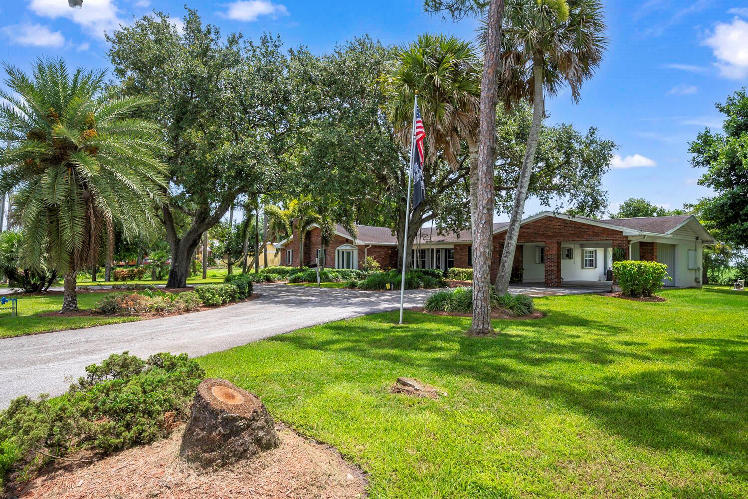 A single-story brick house with a paved driveway, large trees, and a flagpole — 13348 Us Highway 441, Canal Point FL 33438, CANAL POINT, FL