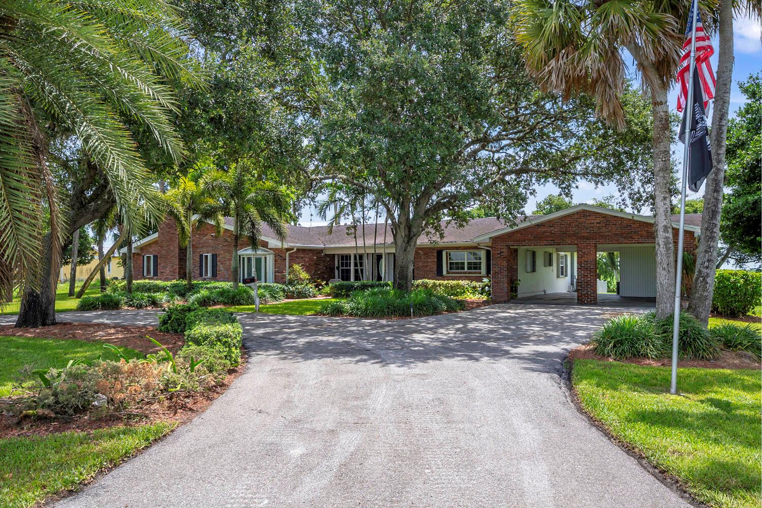 A brick ranch-style house with a large driveway, mature trees, and a covered carport — 13348 Us Highway 441, Canal Point FL 33438, CANAL POINT, FL