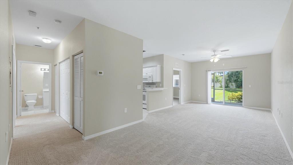 A living room with beige carpet, a ceiling fan, and an adjacent kitchen area — 3958 MEDITERRANEA CIRCLE UNIT 411, SARASOTA, FL