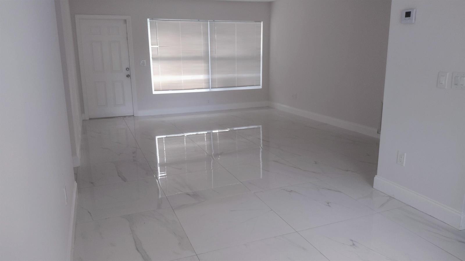 An empty room features white marble-look tile flooring, light gray walls, and a large window — 22682 Family Circle, Boca Raton FL 33428, BOCA RATON, FL
