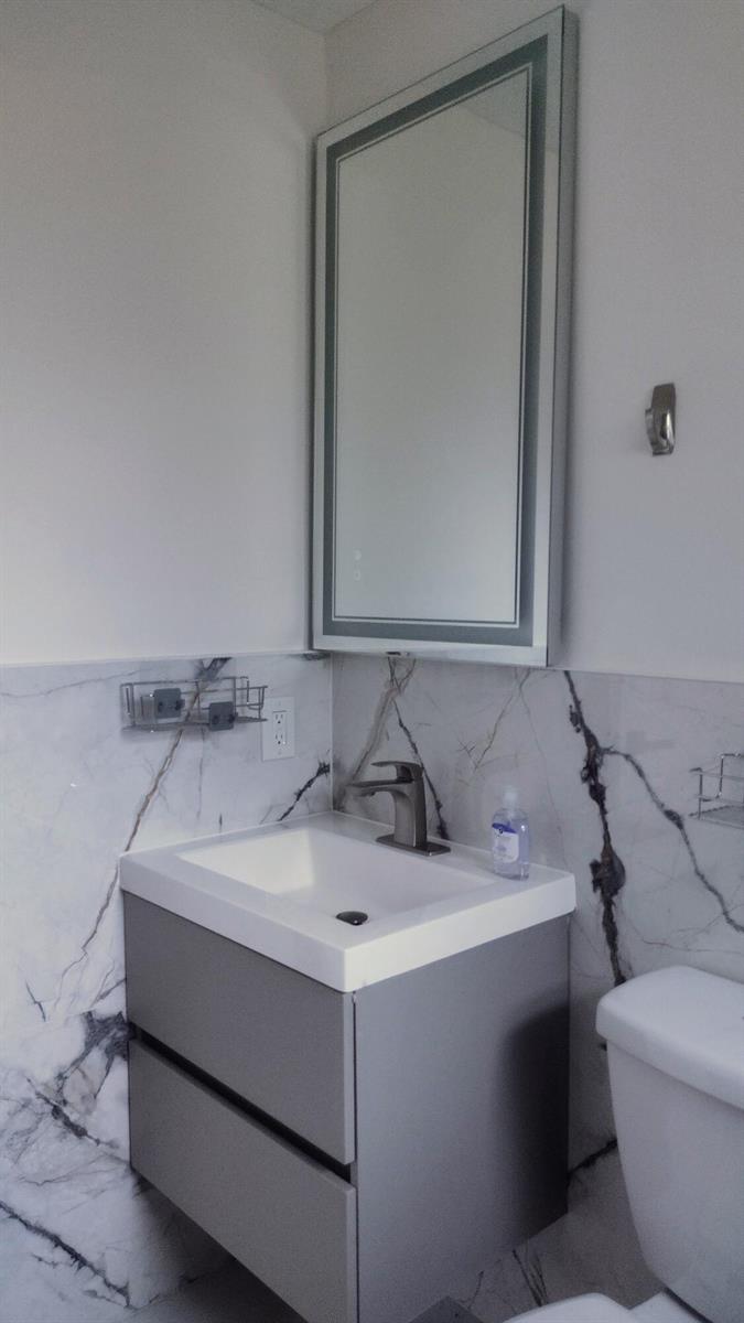 A bathroom features a gray floating vanity, a white sink, and white marble-patterned wall tiles — 22682 Family Circle, Boca Raton FL 33428, BOCA RATON, FL