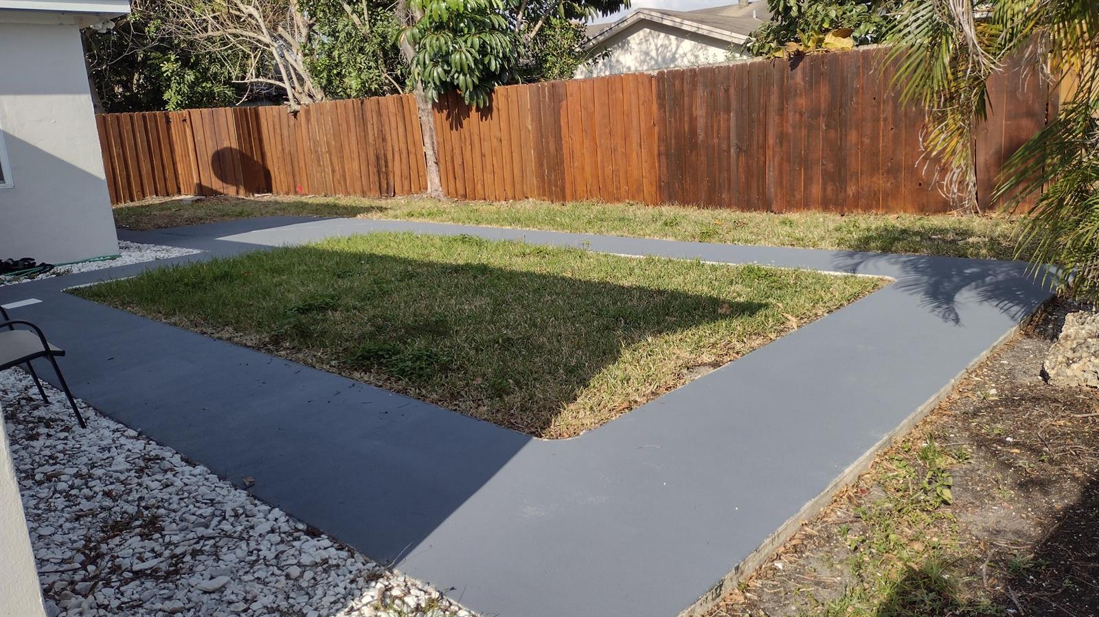 A backyard features a rectangular grass lawn bordered by a smooth, gray concrete walkway — 22682 Family Circle, Boca Raton FL 33428, BOCA RATON, FL