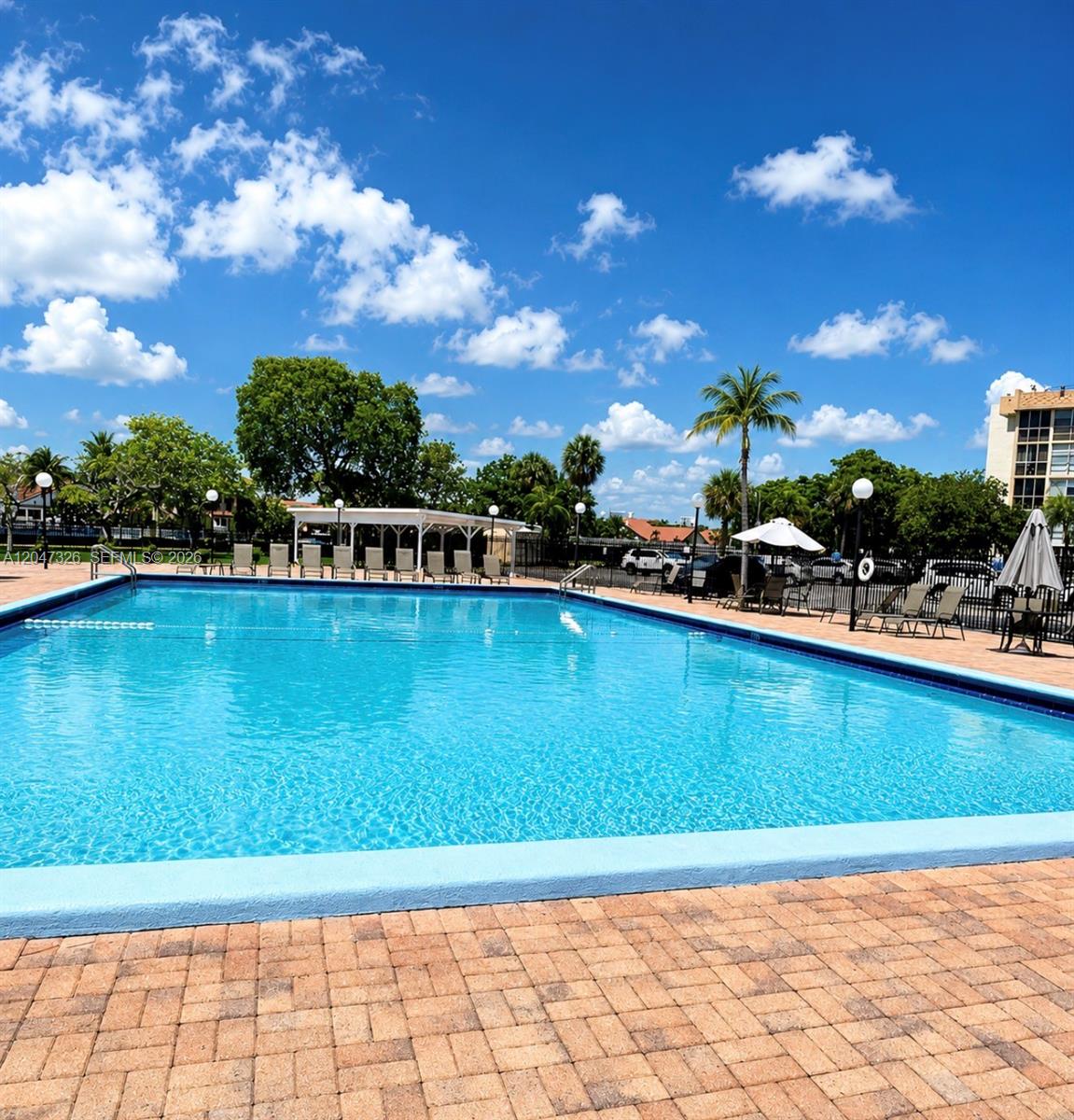 A rectangular swimming pool is surrounded by a brick patio, lounge chairs, and palm trees — 801 Three Islands Blvd # 107, Hallandale Beach FL 33009, HALLANDALE BEACH, FL