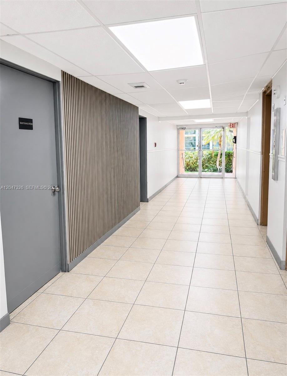A hallway with tile flooring, a slatted wood accent wall, and a glass exit door — 801 Three Islands Blvd # 107, Hallandale Beach FL 33009, HALLANDALE BEACH, FL