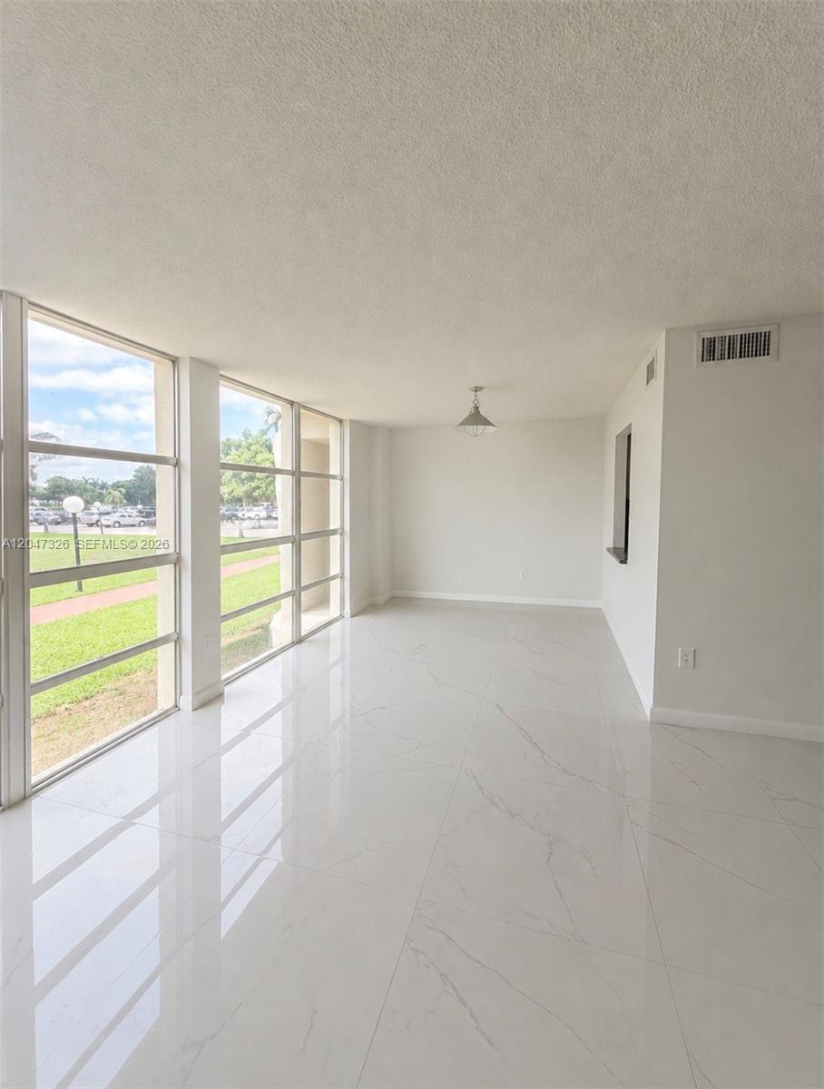 An empty room features white marble-look tile flooring, large windows, and a single pendant light — 801 Three Islands Blvd # 107, Hallandale Beach FL 33009, HALLANDALE BEACH, FL