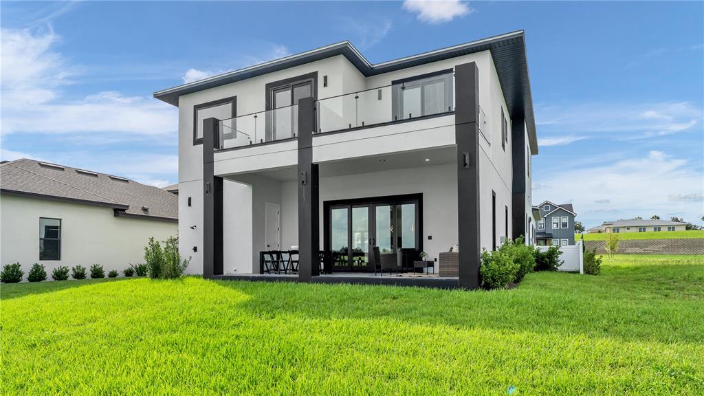 The rear exterior of a modern two-story house features a covered patio and upper balcony — 156 CALADIUM AVENUE, LAKE ALFRED, FL