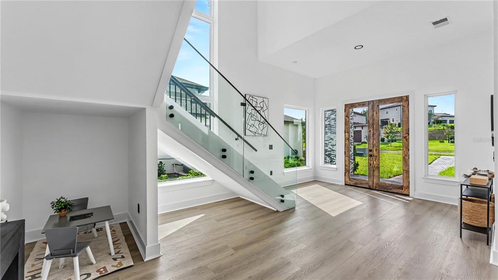 A bright entryway features a modern glass-railed staircase, wood-look flooring, and a children's play area — 156 CALADIUM AVENUE, LAKE ALFRED, FL