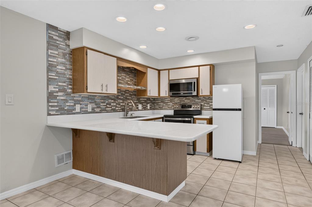 A kitchen features wood-tone cabinets, a white countertop, a tiled backsplash, and a white refrigerator — 4854 RABAMA PLACE, ORLANDO, FL