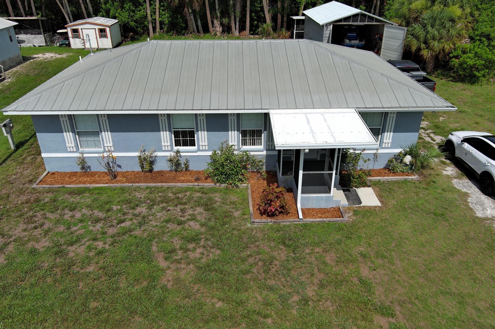 An aerial view of a blue single-story house with a metal roof and landscaping — 1163 Click Drive, Moore Haven FL 33471, MOORE HAVEN, FL