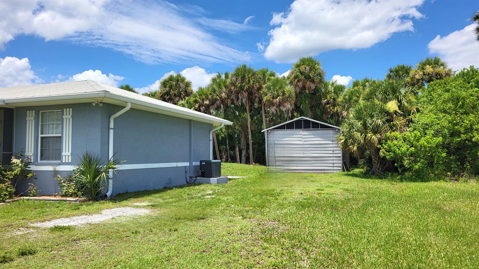 A gray house exterior with a metal shed in the backyard surrounded by palm trees — 1163 Click Drive, Moore Haven FL 33471, MOORE HAVEN, FL