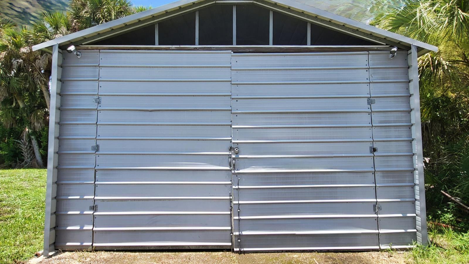 A metal storage shed with double doors stands in a grassy area with palm trees — 1163 Click Drive, Moore Haven FL 33471, MOORE HAVEN, FL