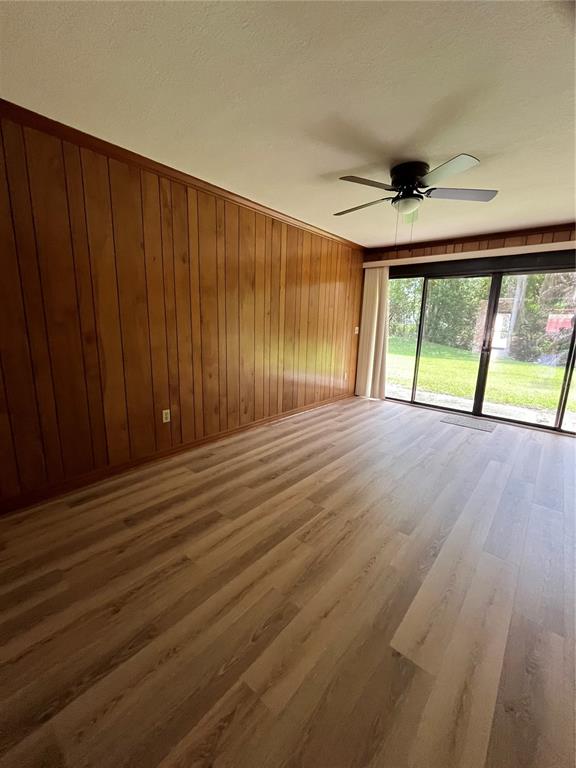 A room with wood-paneled walls, light wood-look flooring, a ceiling fan, and sliding glass doors — 1052 MEDINAH DRIVE, WINTER HAVEN, FL