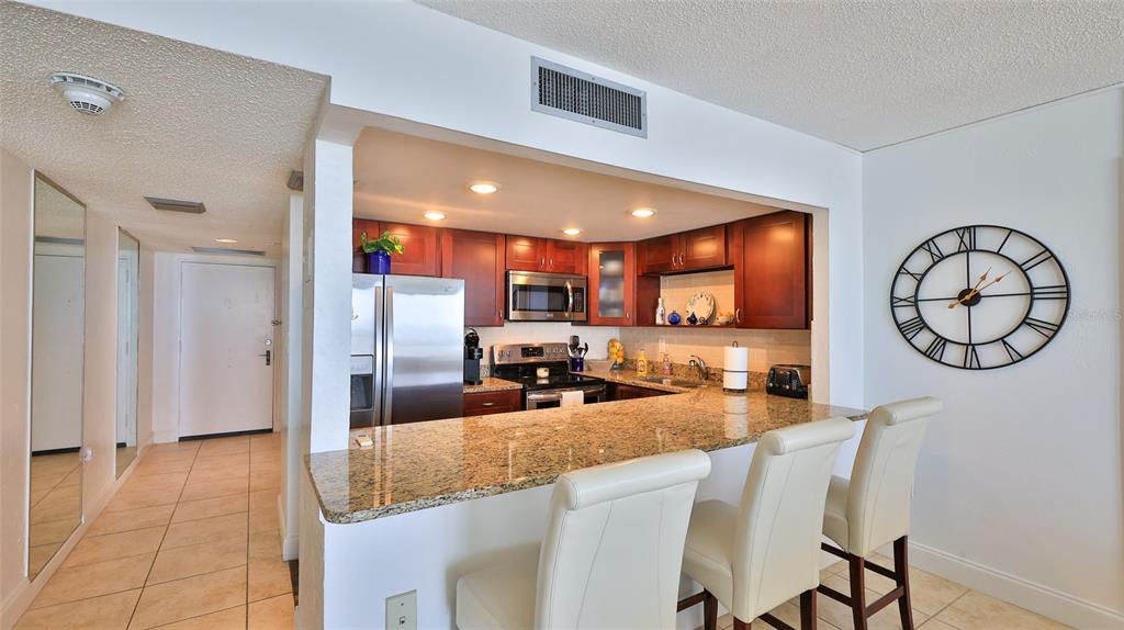 A kitchen with dark wood cabinets, granite countertops, and a breakfast bar with three chairs — 3051 S ATLANTIC AVENUE UNIT 2206, DAYTONA BEACH, FL
